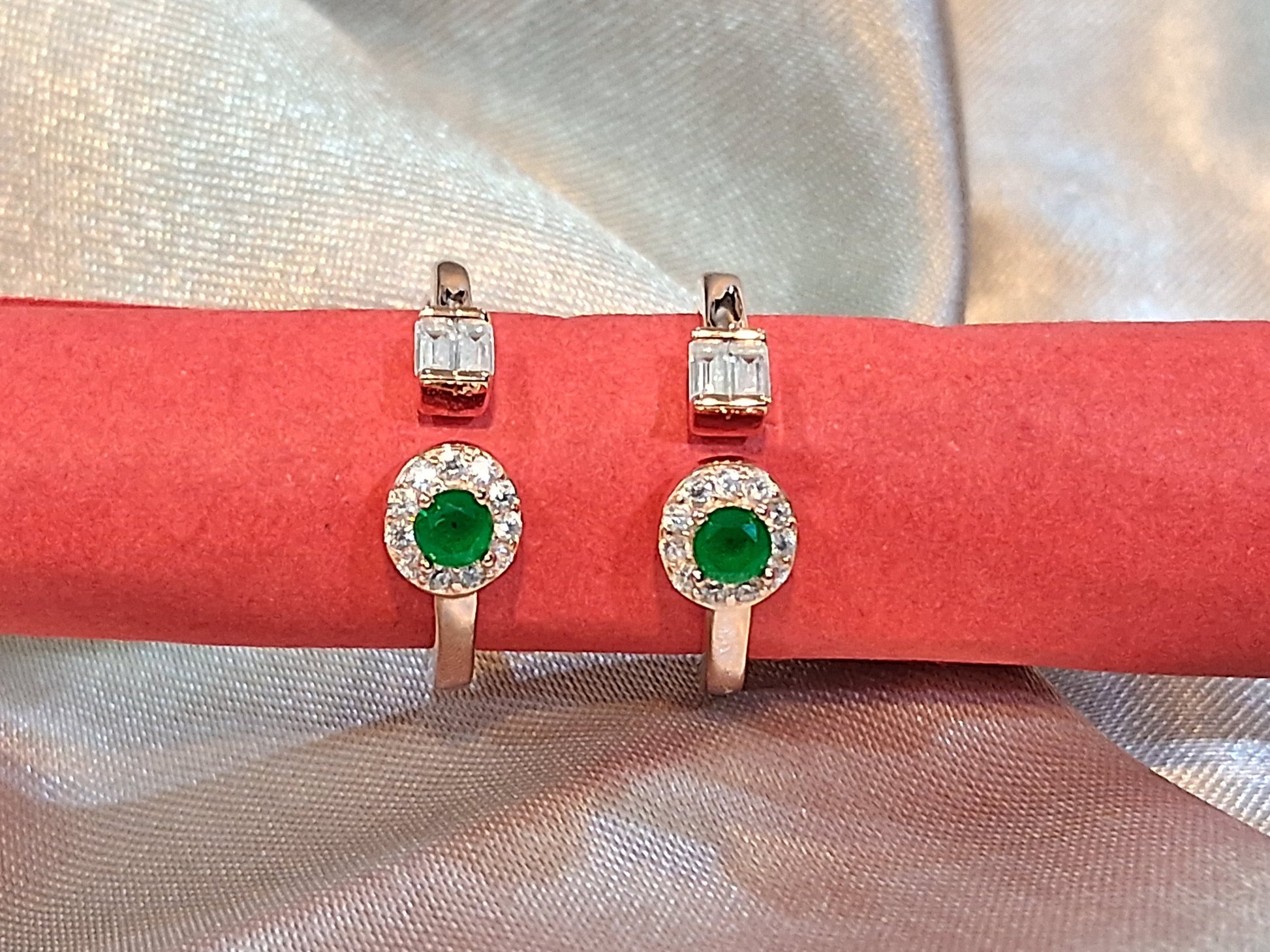 Pair of toerings with green gemstones on a red cushion against a light fabric background