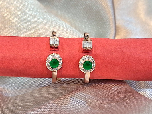 Pair of toerings with green gemstones on a red cushion against a light fabric background