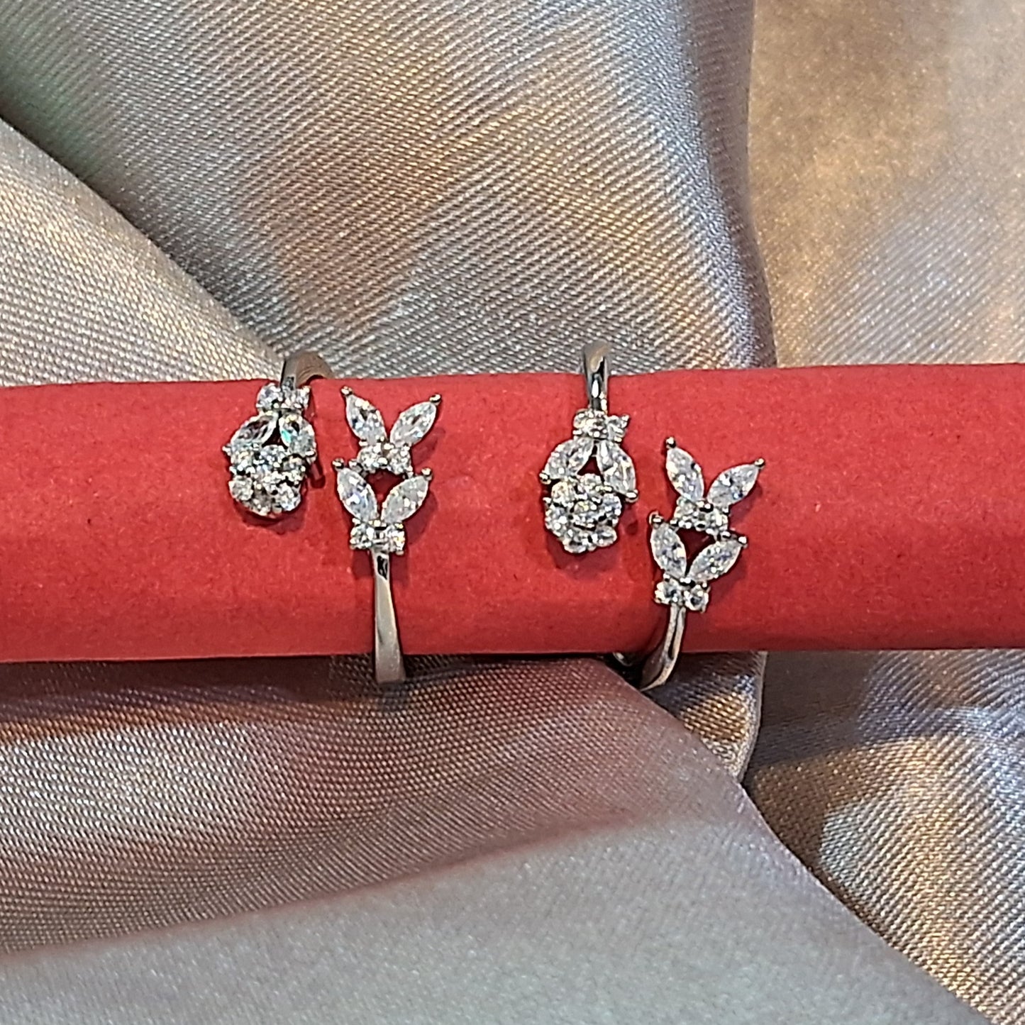 Pair of silver toerings on a red stick against a beige fabric background